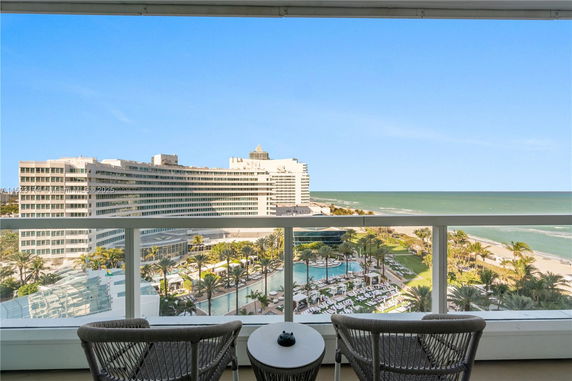 Panoramic view from a balcony overlooking a beachfront resort with a swimming pool and ocean.