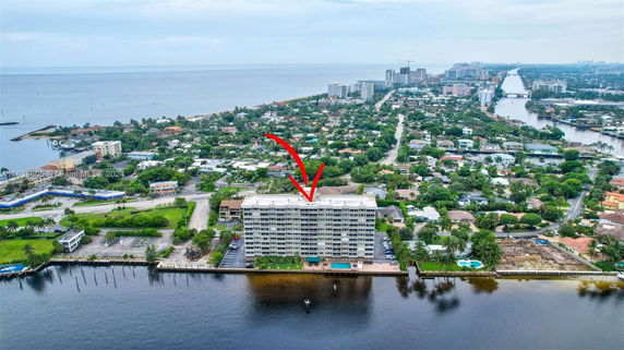 Aerial view of a multi-story building by the water with surrounding neighborhood and coastline.