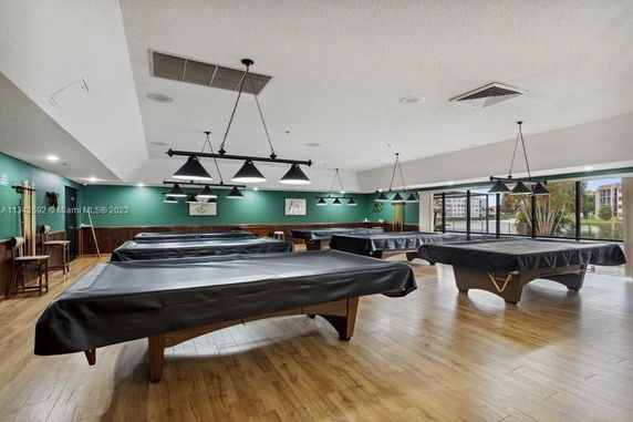Room with multiple billiard tables covered with black cloths, green walls, and hanging ceiling lights.