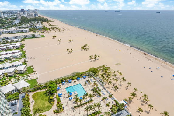 Panoramic view of a beach with adjacent buildings and a swimming pool area.