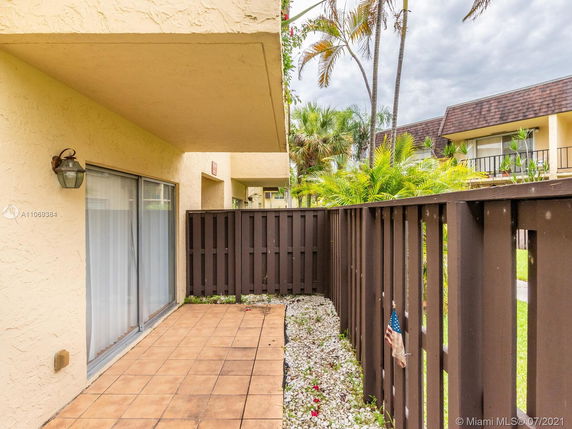 Outdoor patio area of a residential building with a tiled floor, sliding glass door, and surrounding fence.