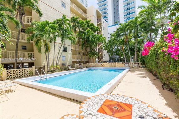 Outdoor area with a swimming pool surrounded by buildings and palm trees.