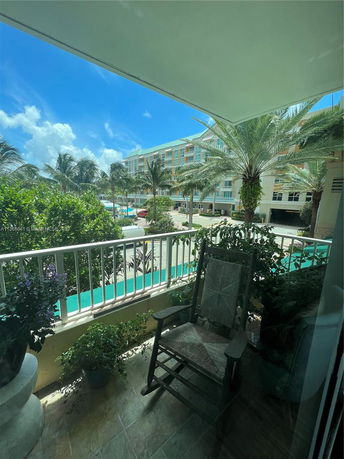 View from a balcony overlooking a multi-story building with a pool and palm trees.