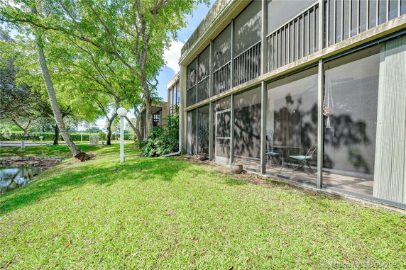 Exterior view of a building with screened balconies surrounded by grass and trees.