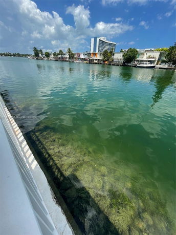 View across a body of water towards several buildings and houses along the shoreline.