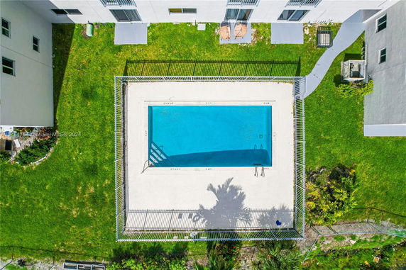Aerial view of a rectangular swimming pool surrounded by grass and a building.