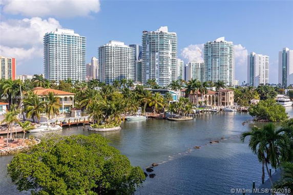View of high-rise buildings and waterfront houses along a canal lined with palm trees.