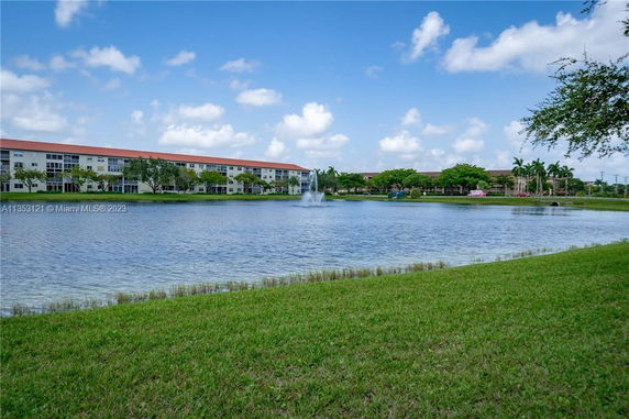 View of a multi-story residential building across a lake with a fountain.