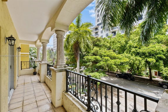View from a balcony overlooking a street lined with trees and adjacent buildings.