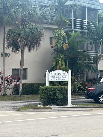 Front view of a residential building with palm trees and a sign displaying street addresses.
