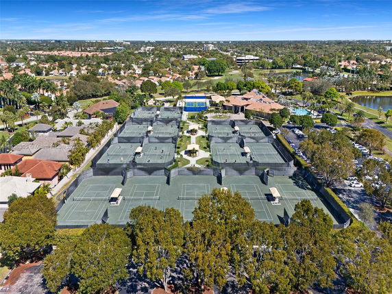 Aerial view of multiple tennis courts located in a residential area with houses and greenery visible in the background.
