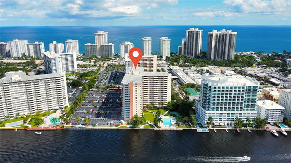 Aerial view of multiple high-rise residential buildings near a body of water, with a highlighted building in the center.
