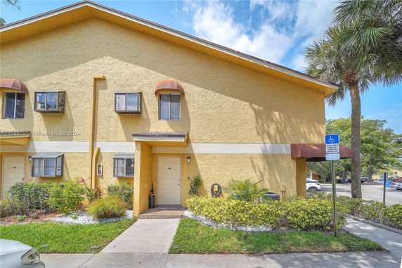 Front view of a two-story townhouse with yellow exterior and multiple windows.