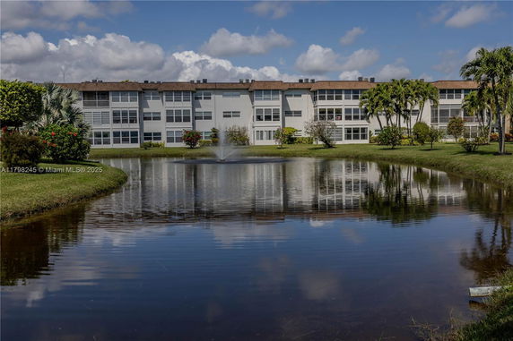 Front view of a three-story apartment building with a pond and fountain in the foreground.