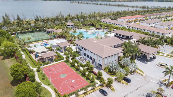 Aerial view of a residential community with sports courts, a swimming pool, and landscaped surroundings near a lake.