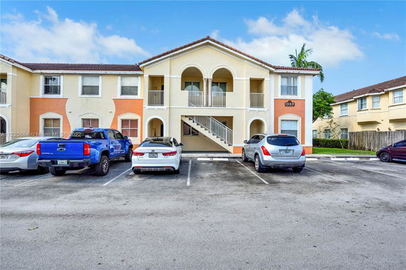 Front view of a two-story residential building with arched balconies and a parking area.
