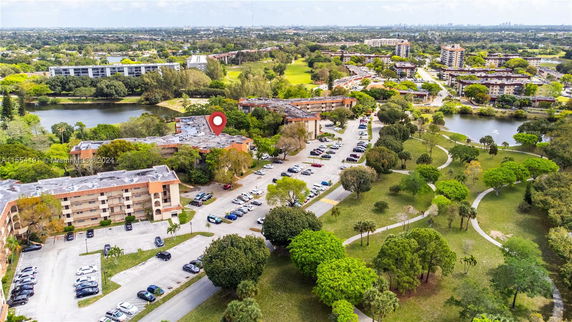Aerial view of a residential complex with a parking area and surrounding greenery and lakes.