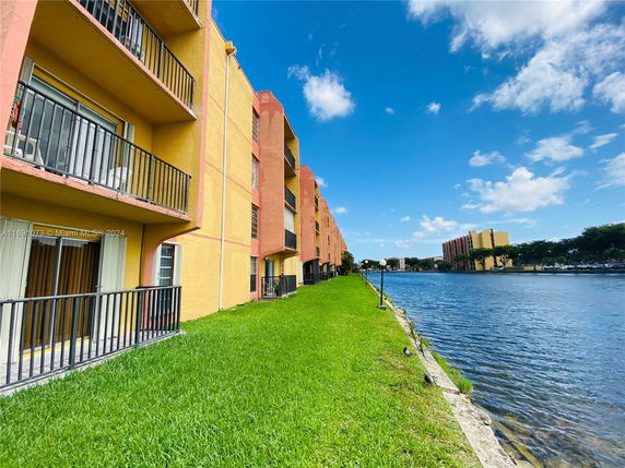 Side view of a multi-story apartment building with balconies overlooking a body of water.