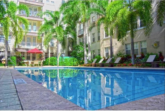 Outdoor swimming pool surrounded by a multi-story building with balconies and palm trees.