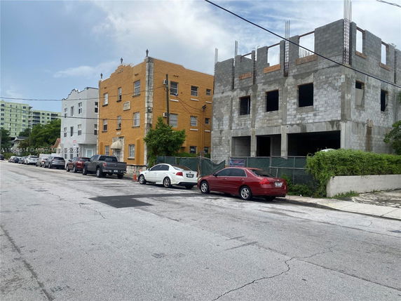 View of building facades, including a multi-story yellow brick building and an adjacent unfinished concrete structure.