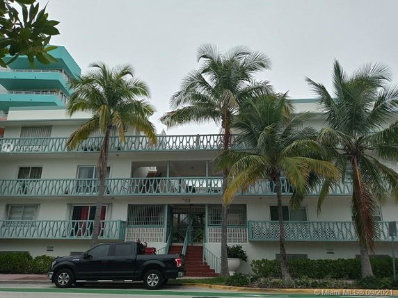 Front view of a multi-story residential building with balconies and palm trees in front.