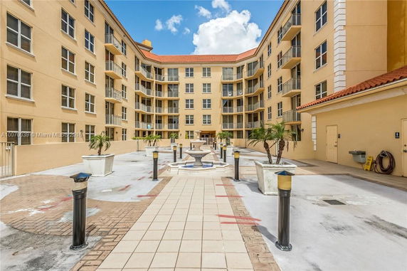 View of a multi-story residential building with balconies and a central courtyard featuring a fountain and planters.