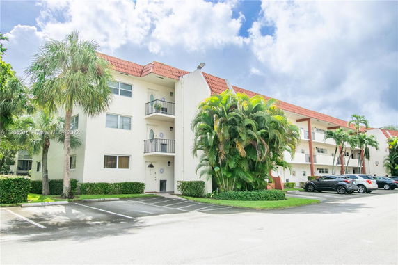 Front view of a multi-story residential building with balconies and a parking area.