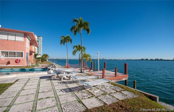 Outdoor area with a view of the waterfront, featuring a pool and palm trees near the edge of a dock.