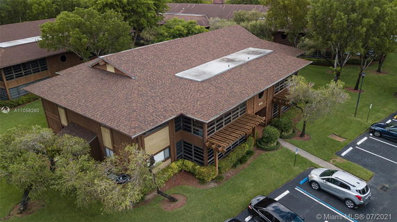 Aerial view of a two-story building with a brown shingle roof and large windows.