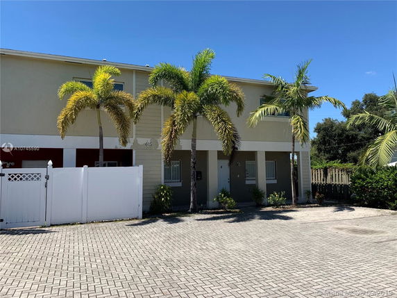 Front view of a two-story building with a paved driveway and palm trees.