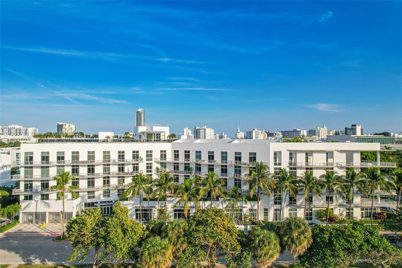 Front view of a multi-story white building with balconies, surrounded by palm trees.