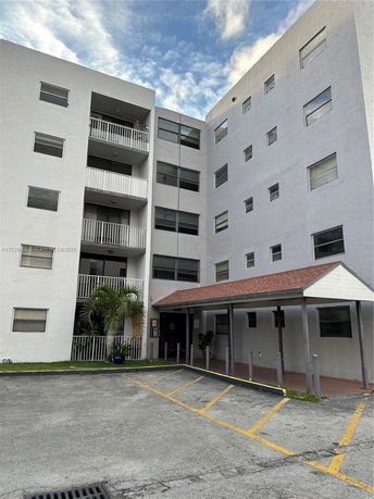Front view of a multi-story apartment building with balconies and a covered entrance.