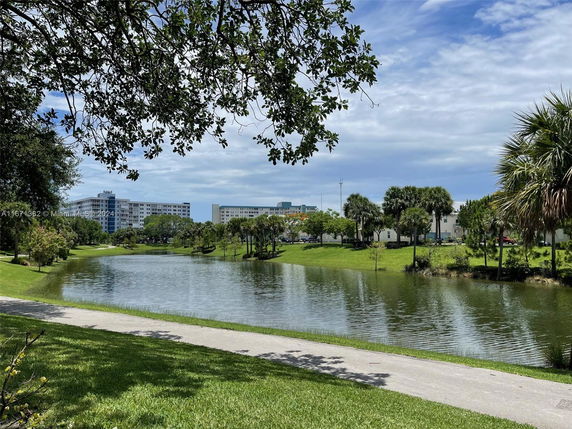 View of buildings across a pond surrounded by greenery and trees.