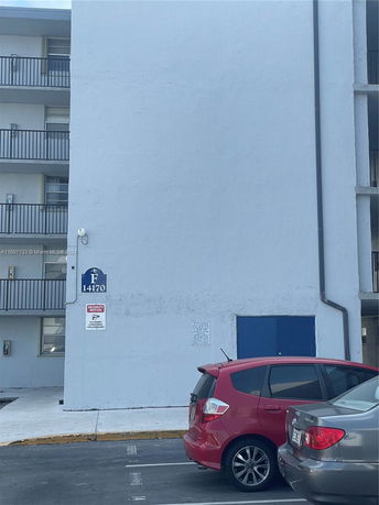 Outdoor view of a multi-story building with parking area and vehicles.