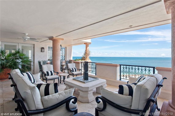 Covered outdoor patio with ocean view, featuring cushioned seating and a central table.
