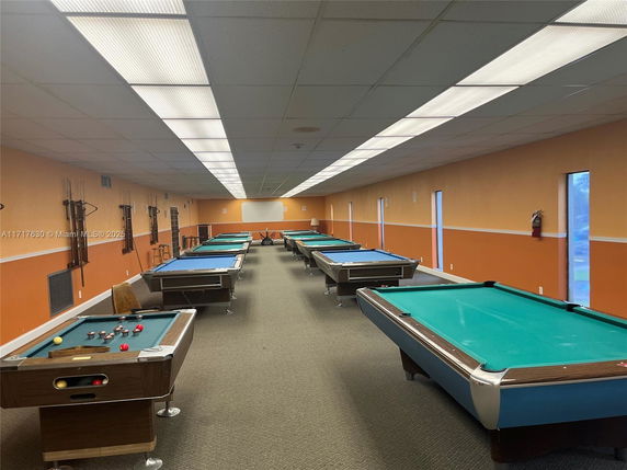 Room with multiple billiard tables and pool cues mounted on the walls.