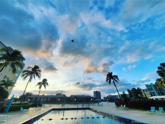 View of a pool area with buildings and palm trees in the background under a cloudy sky