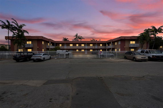 Front view of a two-story building with a gated parking area and a sunset sky in the background.