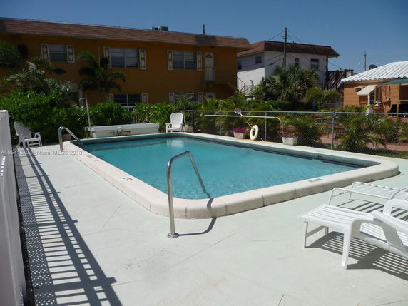 View of a fenced backyard area with a swimming pool and adjacent buildings.