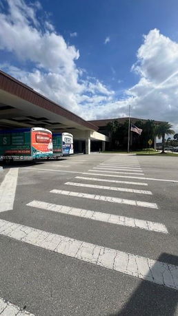 Front view of a building with a large covered area and parked vehicles.
