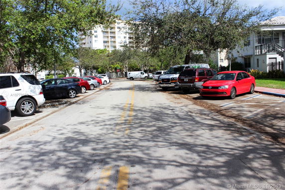 View of parking area with several vehicles and apartments in the background.