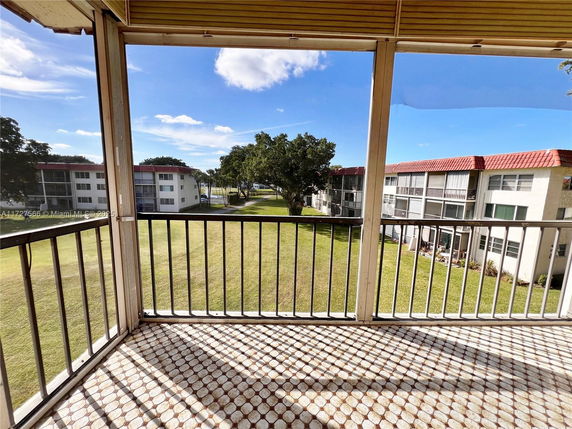 View from a balcony overlooking a grassy area and adjacent apartment buildings.