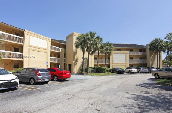 Front view of a multi-story apartment building with balconies and parking area.