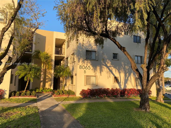 Front view of a multi-story building with windows and entrance, surrounded by trees and plants.