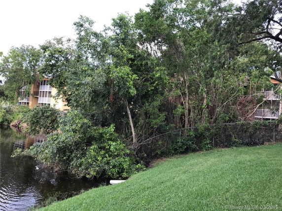 View of buildings partially obscured by trees beside a water body.