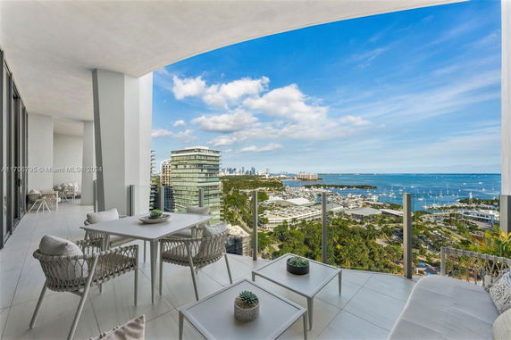 Panoramic view from a high-rise building balcony overlooking a coastal area with modern buildings, marina, and ocean.