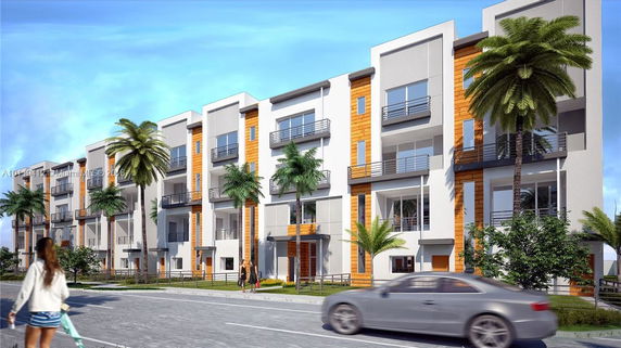 Front view of a modern multi-story apartment building with balconies and palm trees.