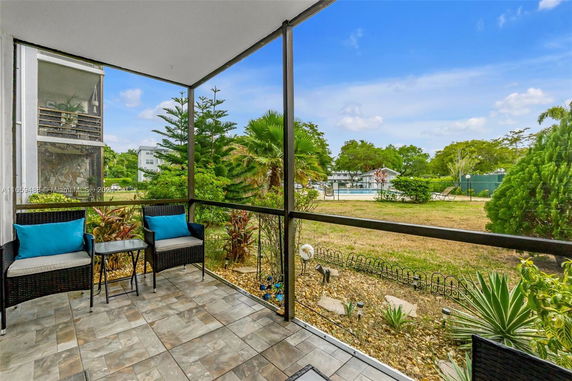 View from a covered patio overlooking a grassy area and a building in the distance.