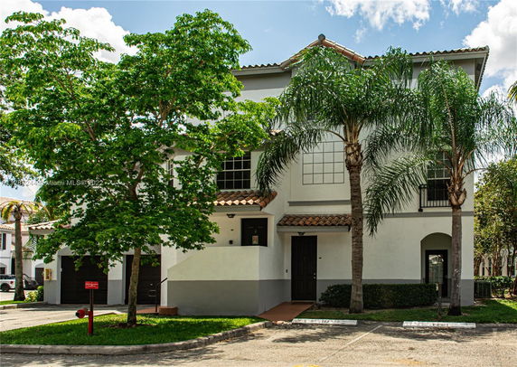 Front view of a multi-story house with tiled roof and palm trees.