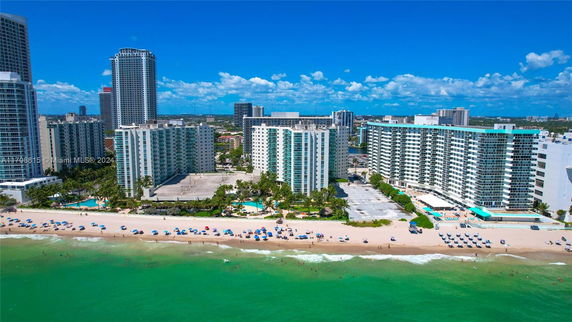 Aerial view of beachfront high-rise buildings with a sandy beach and ocean in the foreground.